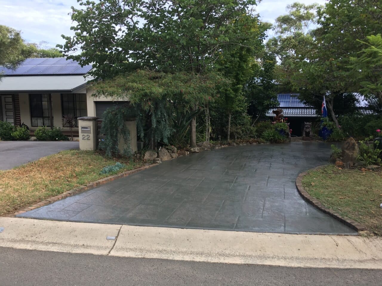 Suburban driveway to house partly hidden by trees, with solar panels and mailbox "22"
