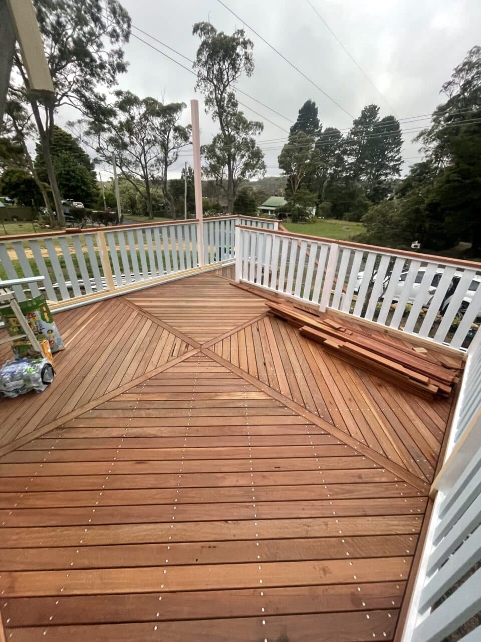 New wooden deck with white railing overlooking grassy yard with trees and wooden planks