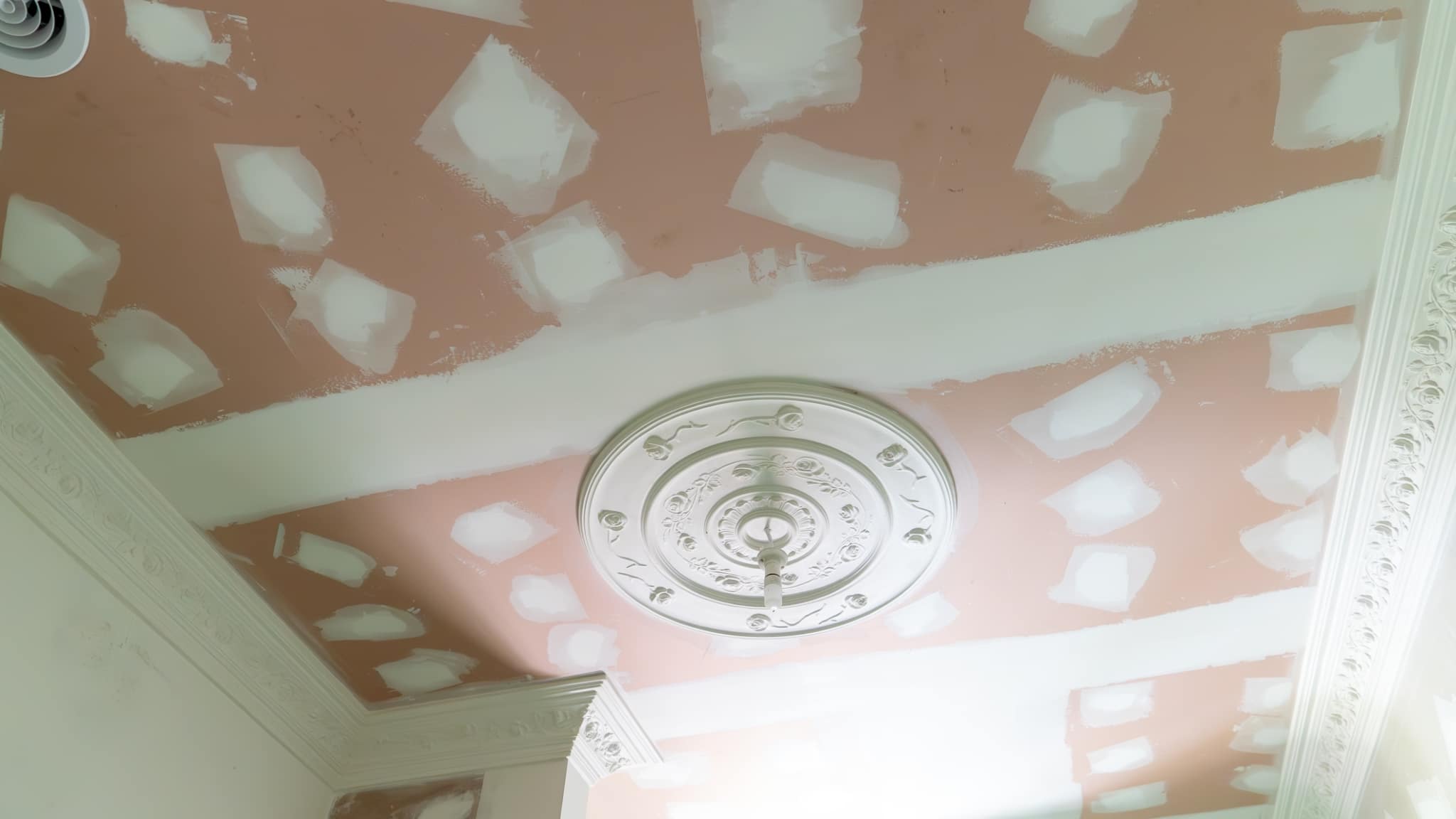 A ceiling under renovation with drywall patches and a partially painted surface