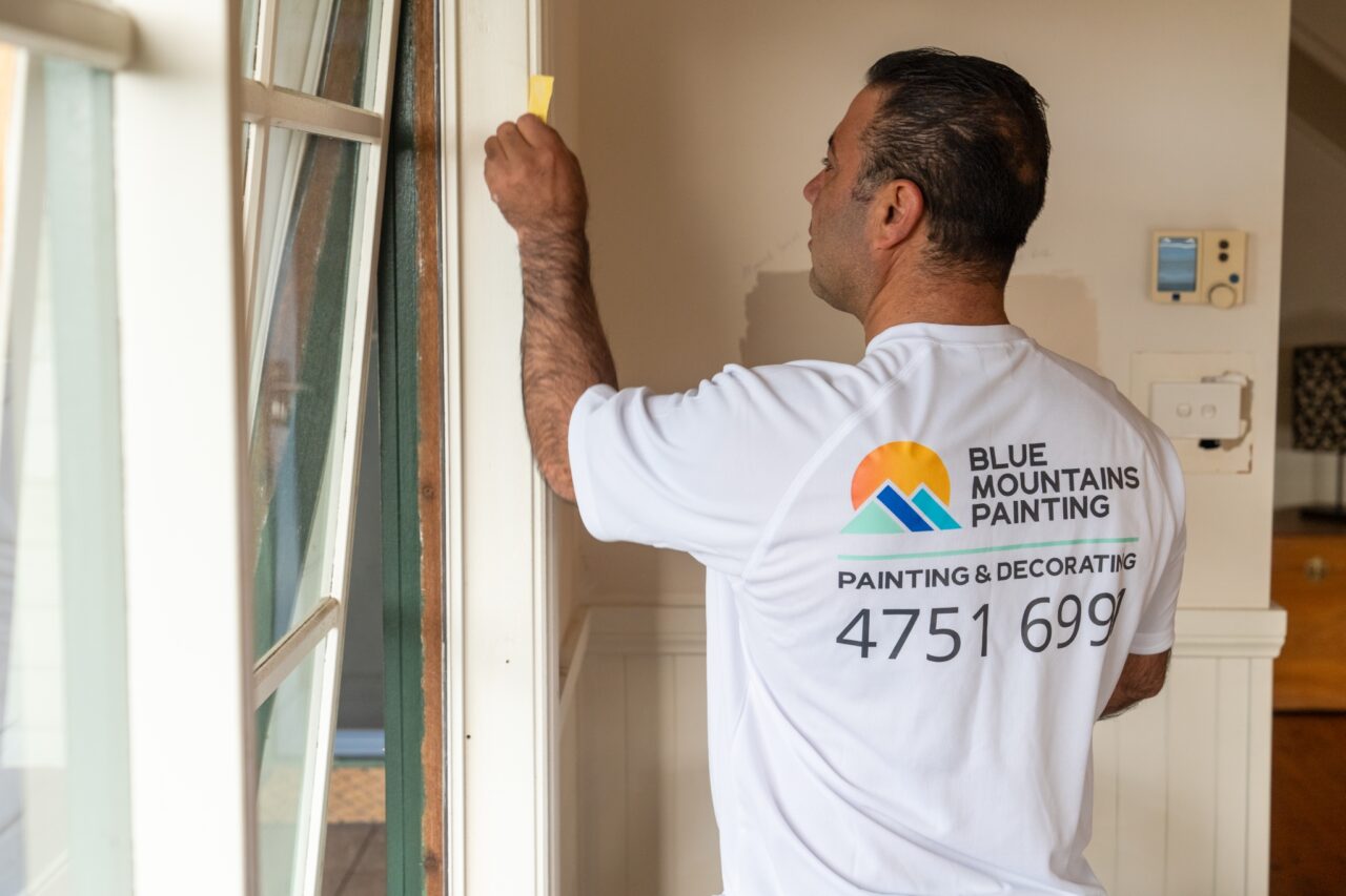 Man wearing a white, Blue Mountains Painting shirt fixing the corner of a window