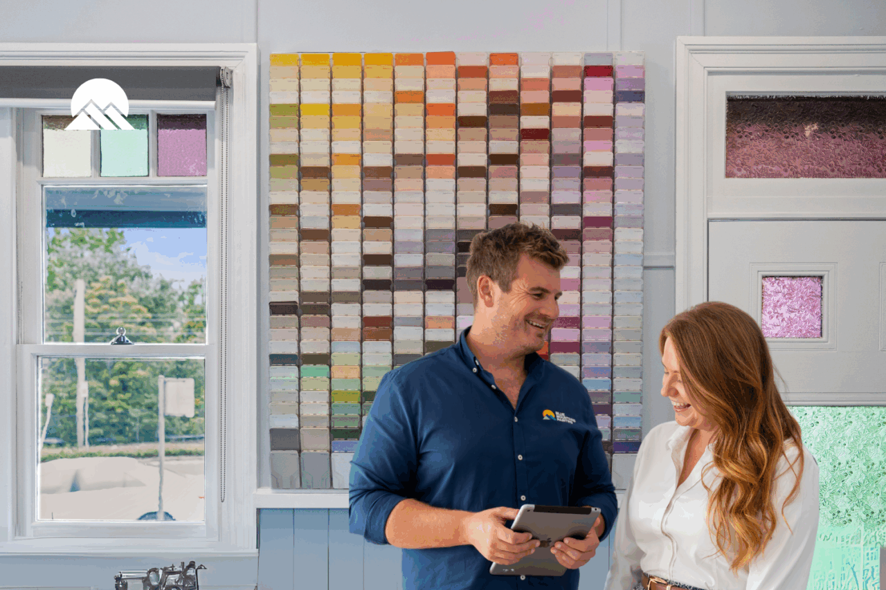 Two people stand in front of a wall covered with paint color swatches, looking at a tablet and smiling in a brightly lit room as they plan painting updates to add value before selling their home.