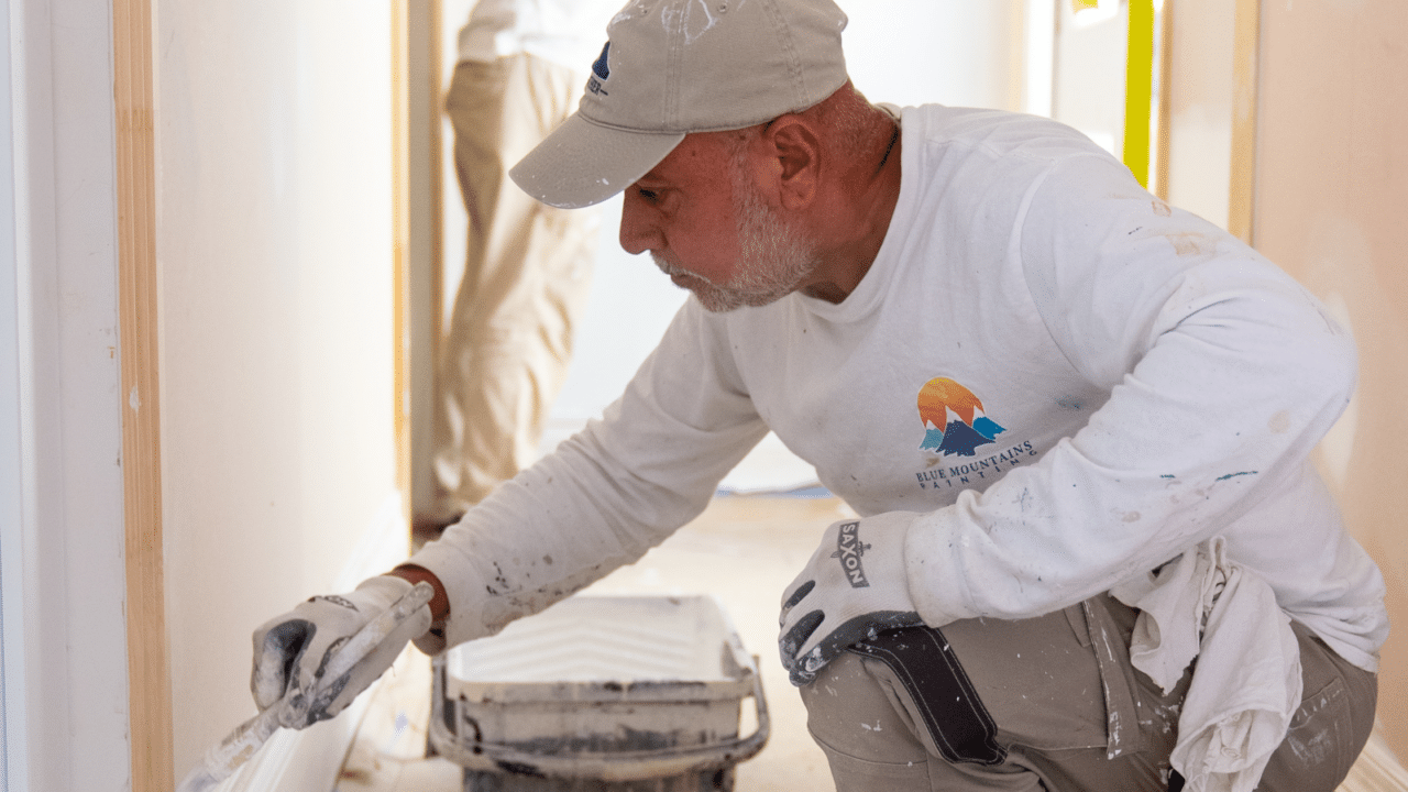 A professional painter in white work clothes and gloves carefully painting a skirting board